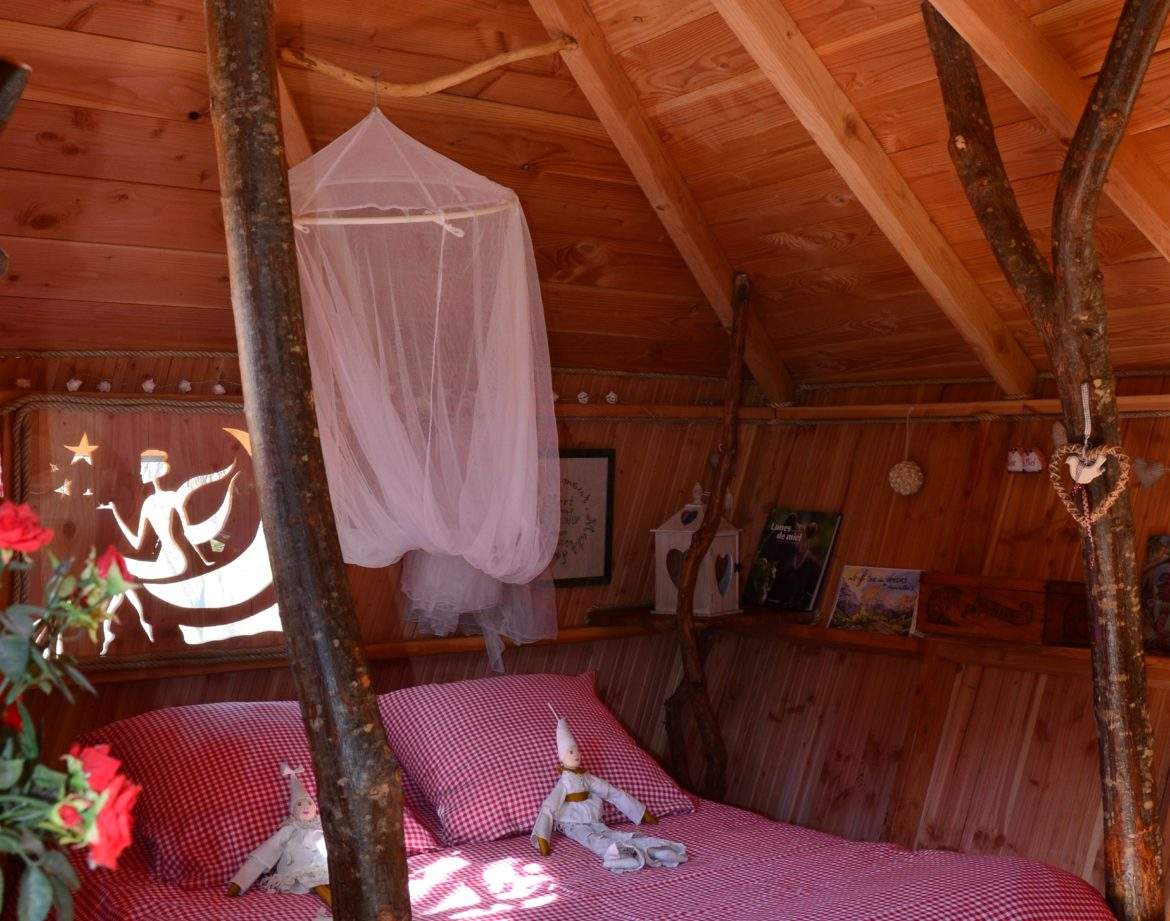 Cabane en bois avec un lit douillet, décorée de branches naturelles et dune ambiance chaleureuse.