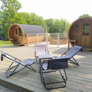 Hébergement insolite en forme de tonneau avec terrasse et chaises longues confortables.