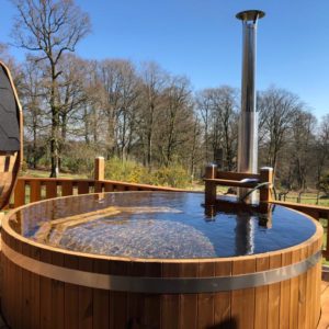 Hébergement insolite en Basse-Normandie avec un jacuzzi en bois entouré de verdure.