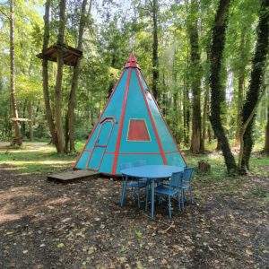 Teepee coloré en pleine forêt, avec une table bleue pour des repas en plein air.
