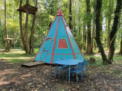 Teepee coloré en pleine forêt, avec une table bleue pour des repas en plein air.