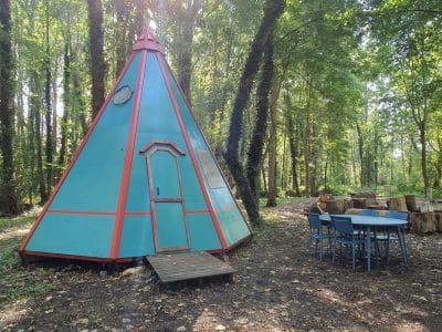 Tipi coloré en pleine forêt, entouré de verdure et dune table en bois.