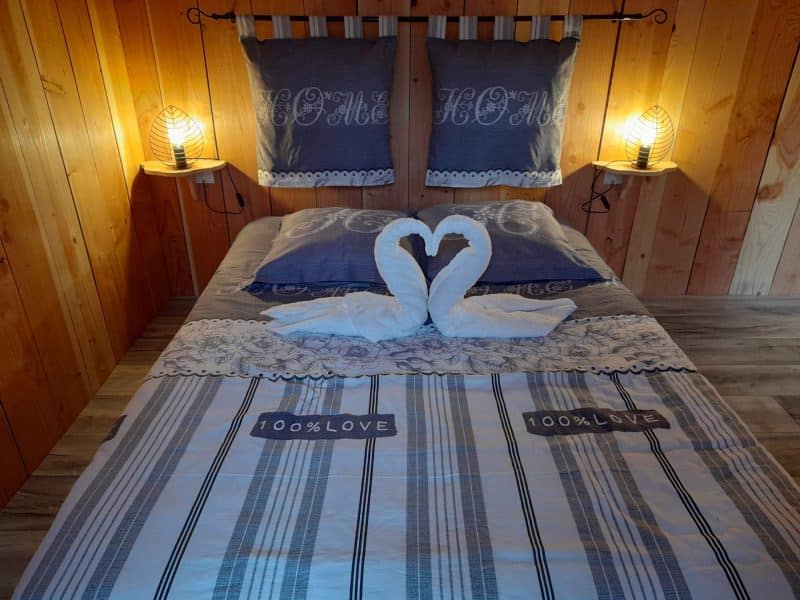 Chalet cosy avec lit douillet et serviettes en forme de cœur sur la couette.