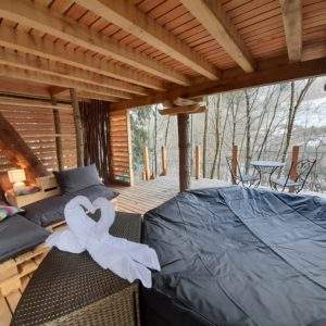 Cabane perchée en bois avec terrasse, coin salon cosy et jacuzzi.