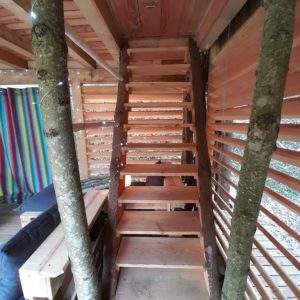 Escalier en bois menant à une cabane perchée, entourée de murs colorés.