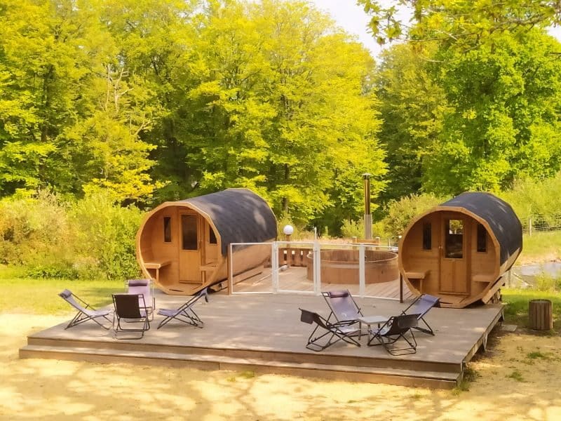 Hébergement en cabanes en bois, avec terrasse et chaises sur un fond verdoyant.