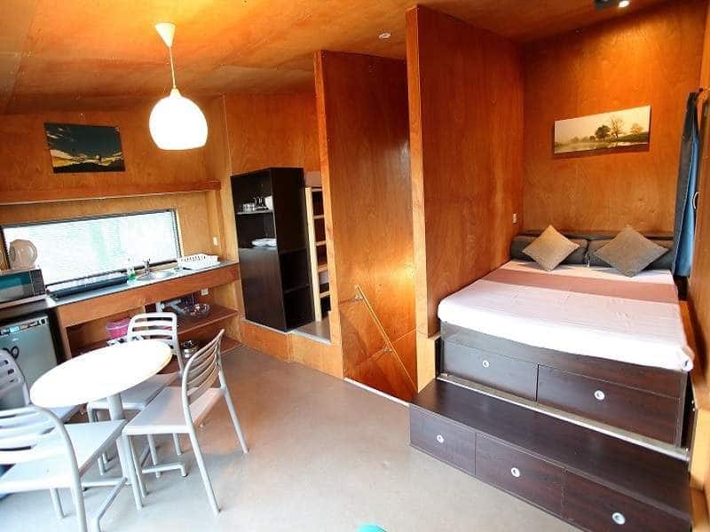 Chalet moderne avec lit double, coin cuisine et table à manger lumineuse.