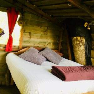 Cabane en bois cosy avec lit douillet et rideaux rouges, au cœur de la nature.