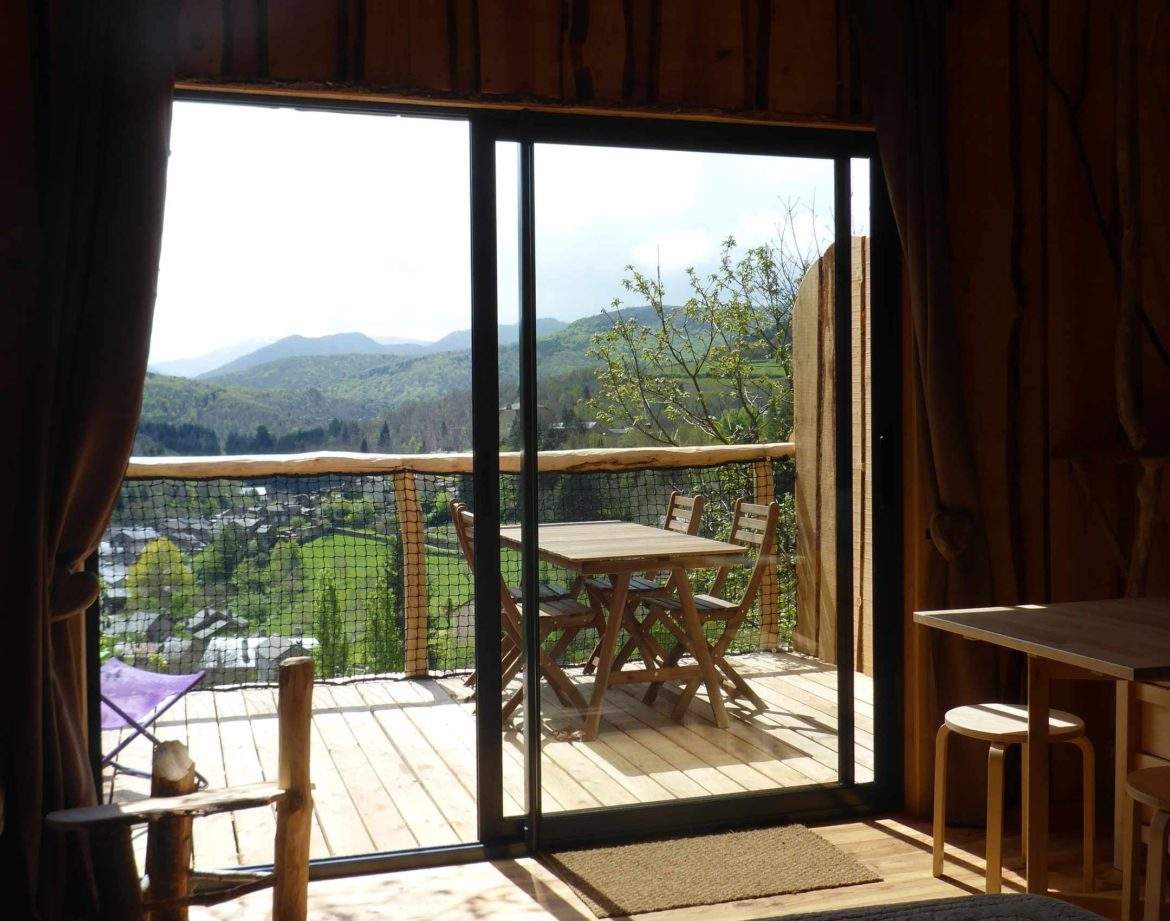 Cabane perchée en bois avec vue sur les montagnes et terrasse ensoleillée.