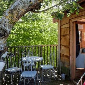 Cabane perchée dans un arbre avec terrasse et mobilier en métal blanc.