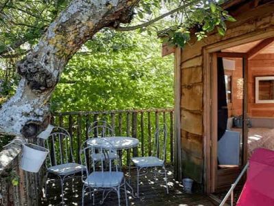 Cabane perchée dans un arbre avec terrasse et mobilier en métal blanc.