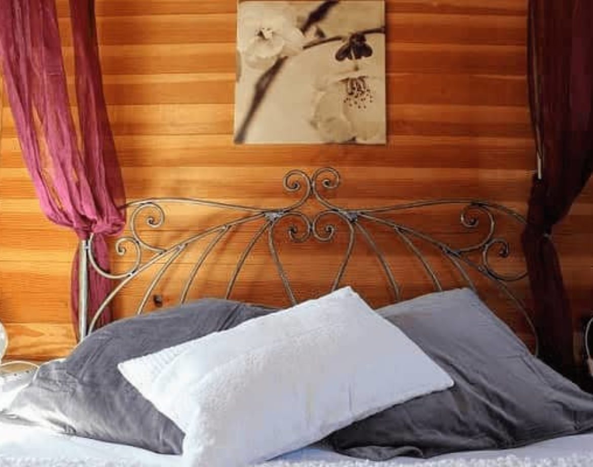Chambre romantique en bois avec lit en fer forgé et coussins moelleux.