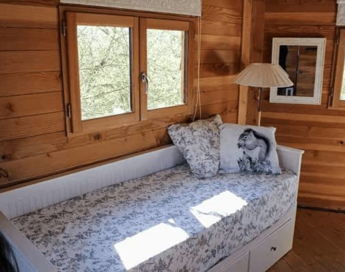 Chalet en bois avec lit confortable et grandes fenêtres laissant entrer la lumière.