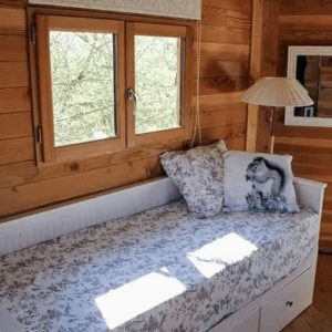 Chalet en bois avec lit confortable et grandes fenêtres laissant entrer la lumière.