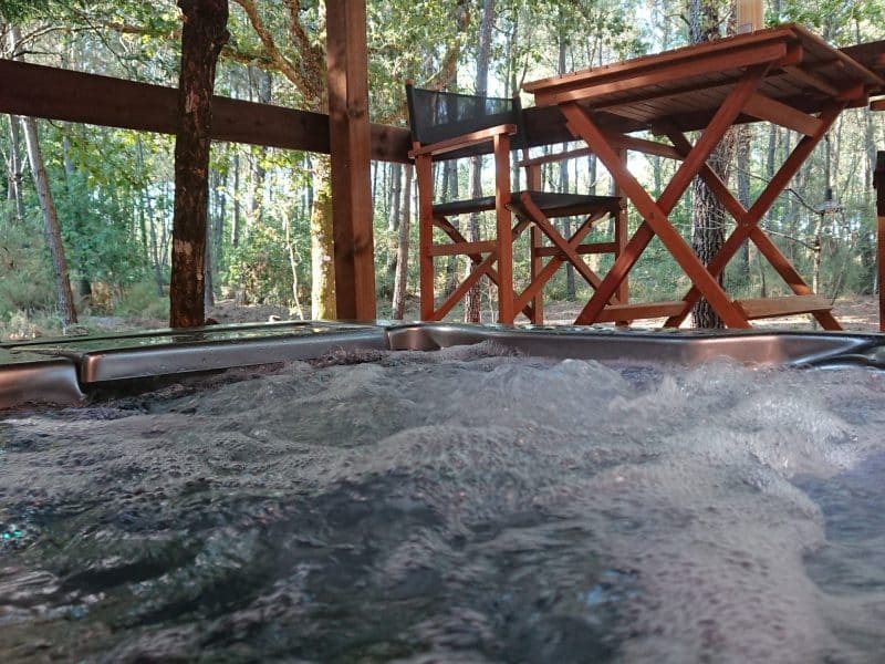 Cabane en bois avec jacuzzi, entourée dune forêt verdoyante.