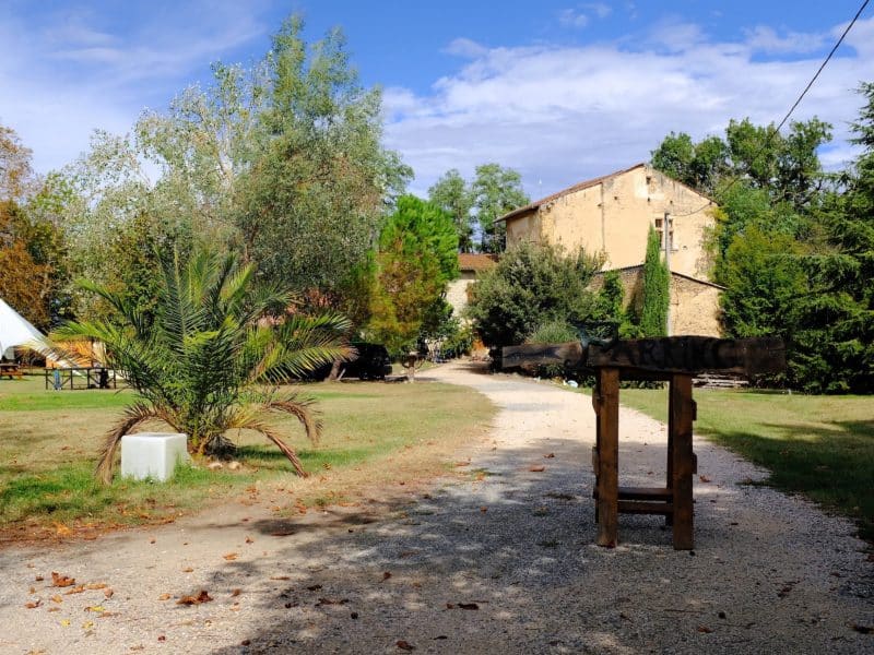 Gîte rural entouré de verdure, avec un chemin menant à un bâtiment en pierre.