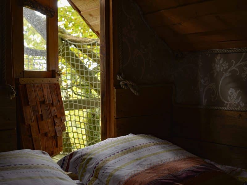 Cabane perchée avec vue sur la nature, décor en bois et literie colorée.