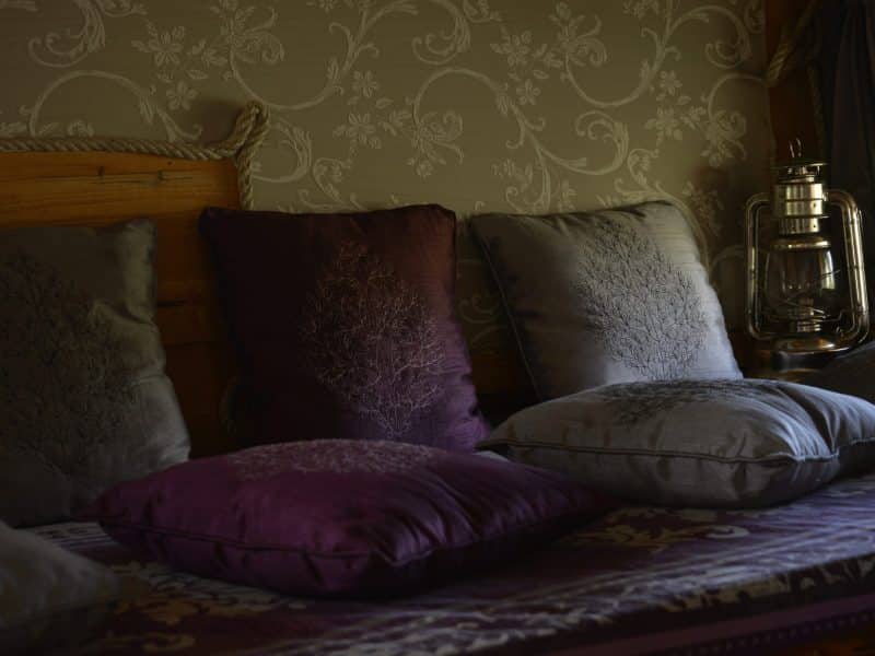 Chambre dhôtes cosy avec coussins colorés et lampe vintage.