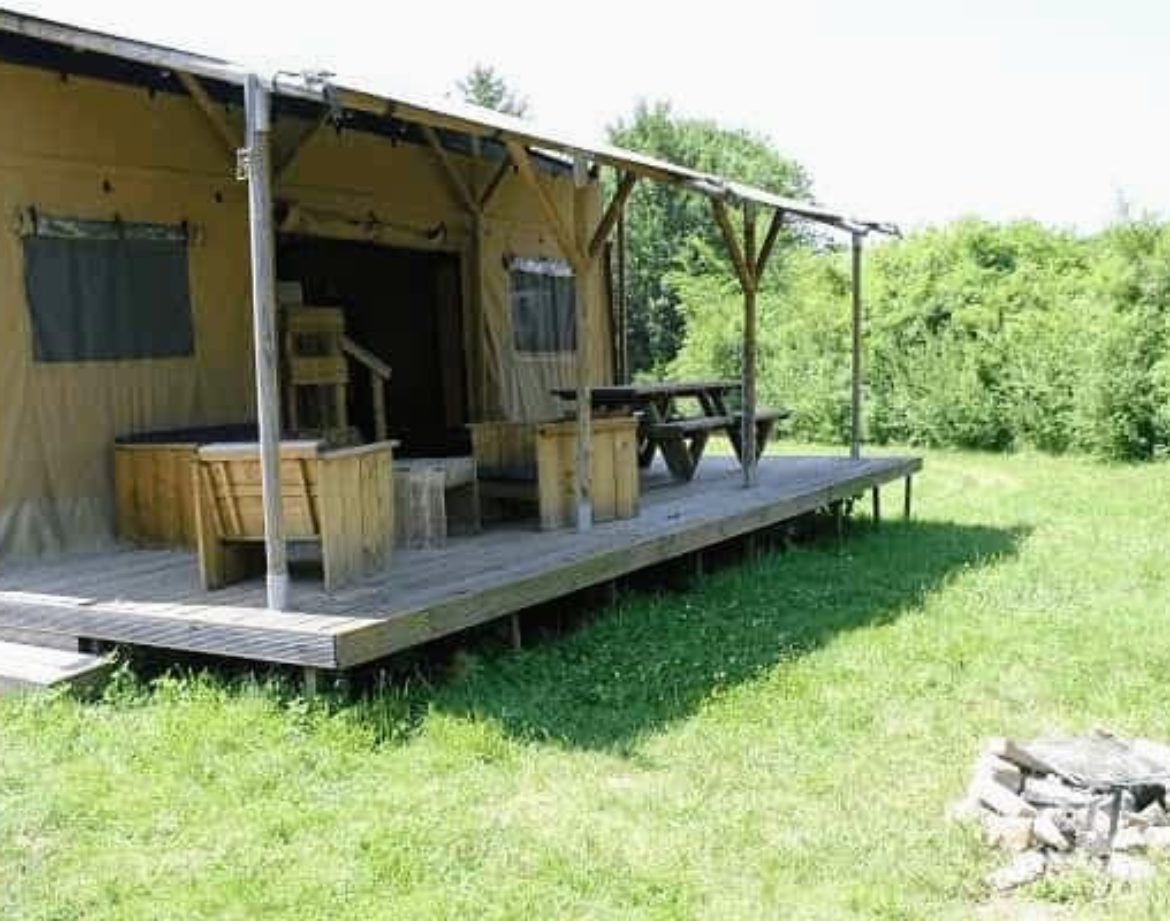 Tente safari spacieuse avec terrasse en bois, entourée de verdure. Parfait pour se ressourcer.