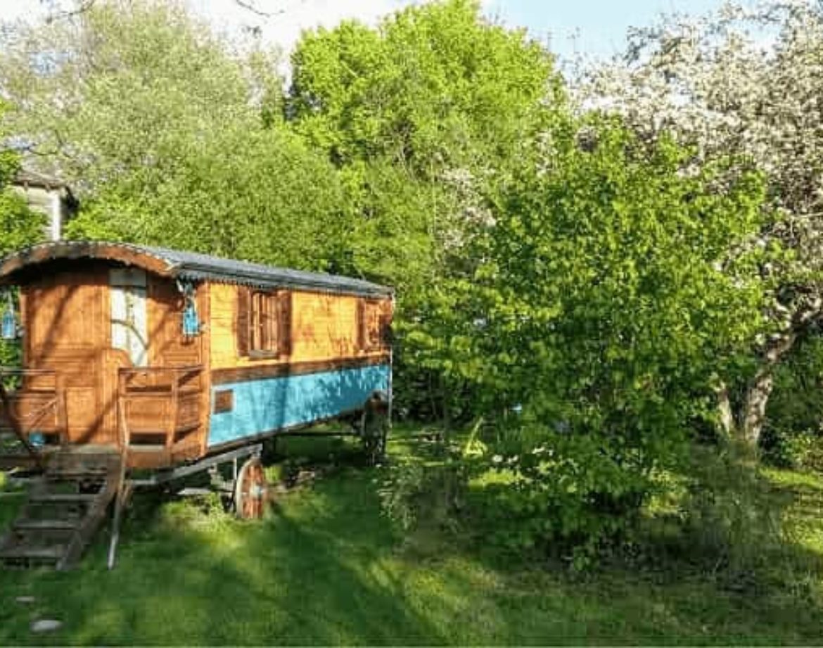 Charmant roulotte en bois, entourée de verdure et darbres fleuris.