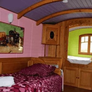 Chalet coloré avec lit douillet et décor en bois, ambiance chaleureuse et originale.