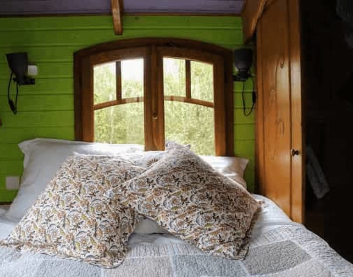 Chalet insolite avec murs verts et coussins décoratifs sur un lit douillet.