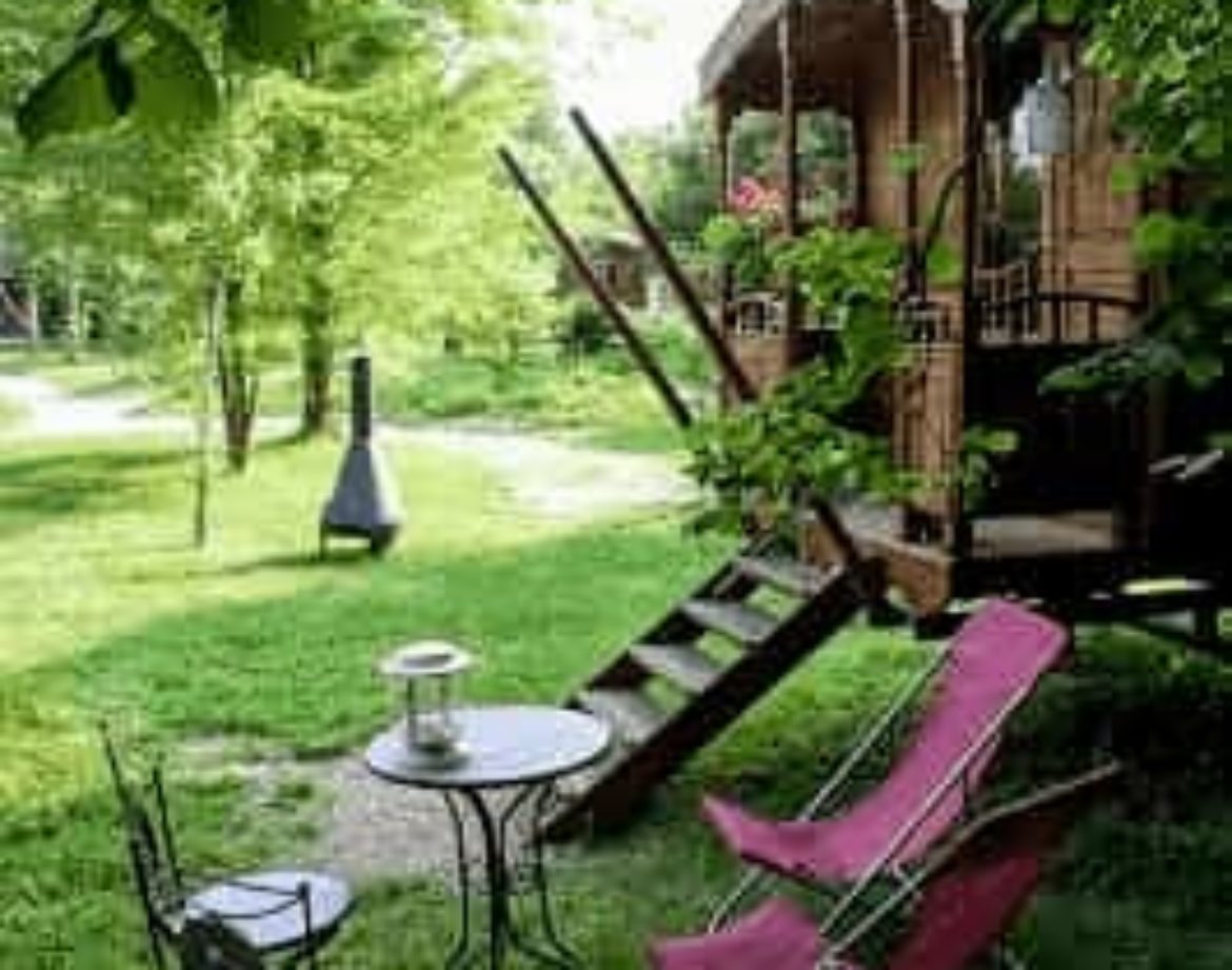 Roulotte charmante avec terrasse, entourée de verdure et mobilier de jardin accueillant.