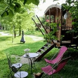 Roulotte charmante avec terrasse, entourée de verdure et mobilier de jardin accueillant.