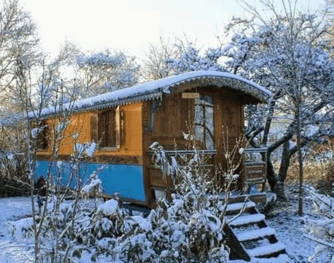 Hébergement insolite : cabane en bois colorée, entourée de neige et darbres.