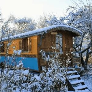 Hébergement insolite : cabane en bois colorée, entourée de neige et darbres.