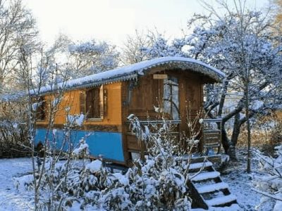 Hébergement insolite : cabane en bois colorée, entourée de neige et darbres.