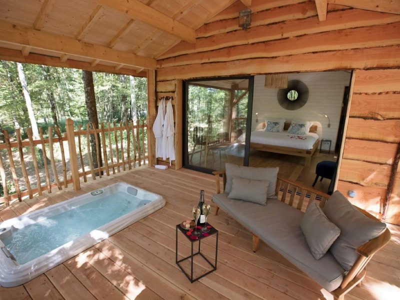 Cabane en bois avec jacuzzi sur la terrasse, entourée de verdure en Aquitaine.