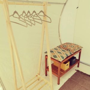 Hébergement insolite en bulle, avec porte-manteaux en bois et coussin coloré.