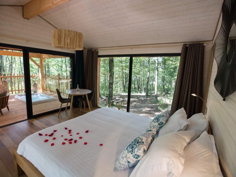 Chalet moderne avec vue sur la forêt, lit décoré de pétales de rose.