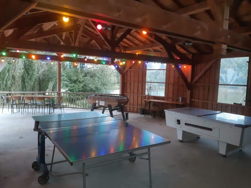Espace de loisirs en hébergement touristique avec tables de ping-pong et lumières colorées.