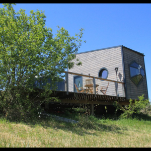 Cabane moderne sur pilotis, avec terrasse en bois et vue dégagée sur la nature.
