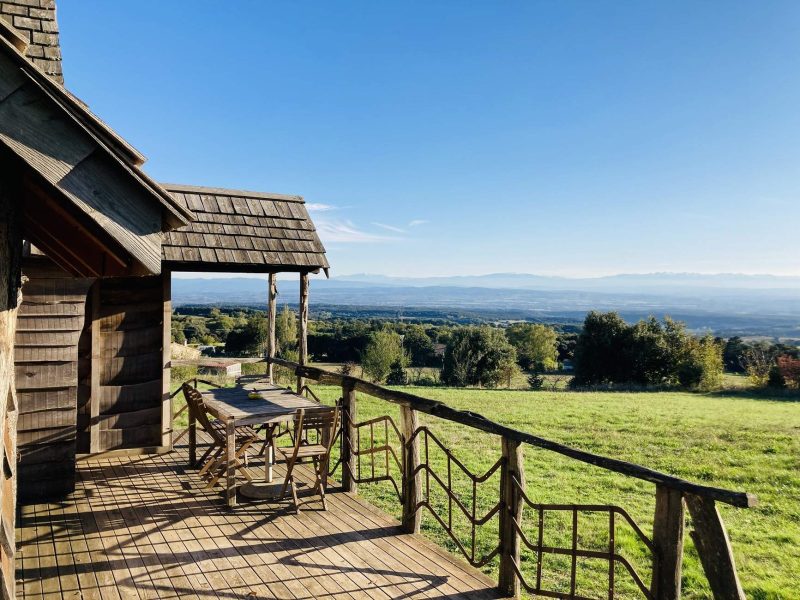 Cabane en bois avec terrasse, vue panoramique sur les montagnes et la nature verdoyante.