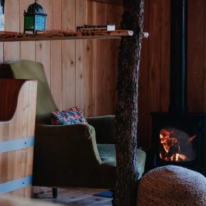 Hébergement insolite en bois avec fauteuil confortable et poêle à bois chaleureux.