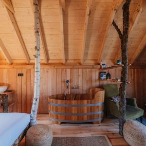 Cabane en bois avec baignoire en bois et cheminée, ambiance chaleureuse et naturelle.