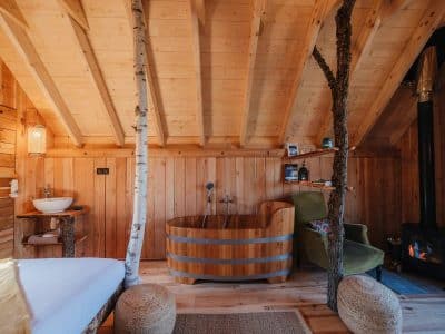 Cabane en bois avec baignoire en bois et cheminée, ambiance chaleureuse et naturelle.