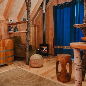 Cabane en bois avec poêle à bois et baignoire en bois, ambiance chaleureuse et naturelle.