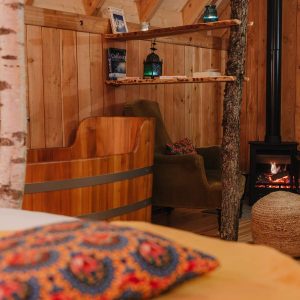 Hébergement insolite en bois avec baignoire en bois et poêle à bois chaleureux.