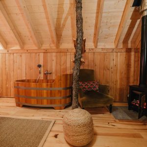 Cabane en bois avec baignoire en bois et poêle à bois, ambiance chaleureuse et naturelle.