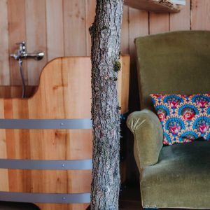 Hébergement insolite en bois avec baignoire en bois et fauteuil vert confortable.
