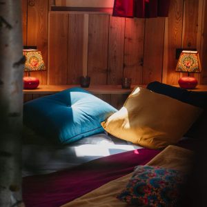 Chalet en bois cosy avec coussins colorés et lampes chaleureuses.