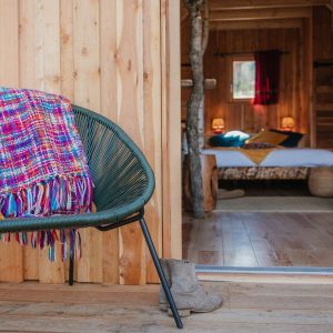 Cabane en bois avec un intérieur chaleureux et un plaid coloré sur un fauteuil.