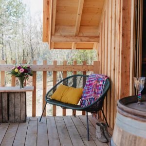 Cabane en bois avec terrasse, fauteuil coloré et bouquet de fleurs. Détente en nature.