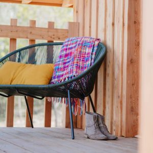 Hébergement insolite en bois avec un fauteuil coloré et une couverture accueillante.