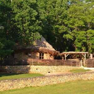 Hébergement insolite en Aquitaine : cabane en pierre avec toit de chaume, entourée de verdure.