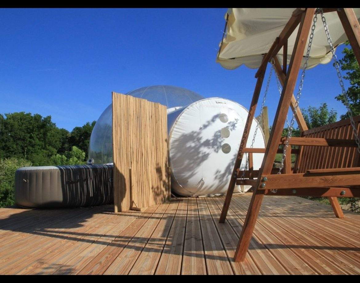 Hébergement insolite en bulle transparente avec terrasse en bois et balancelle.